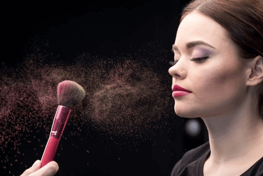makeup artist sprinkling models face with powder with brush